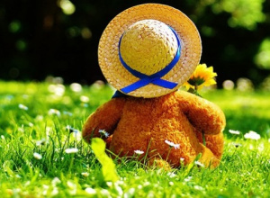Ilustracja dziecka siedzącego tyłem, w słomkowym kapeluszu na letniej łące